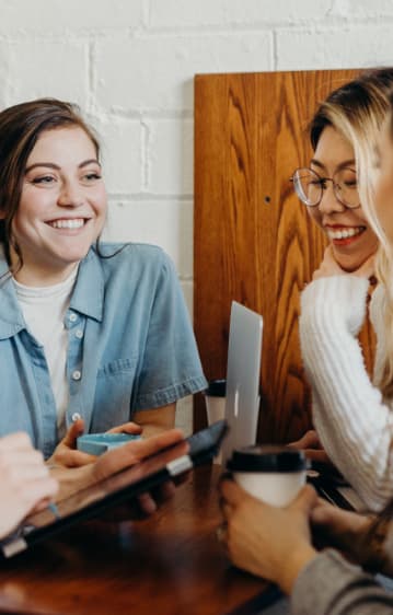 A group of friends sitting together, laughing over coffee and laptops.